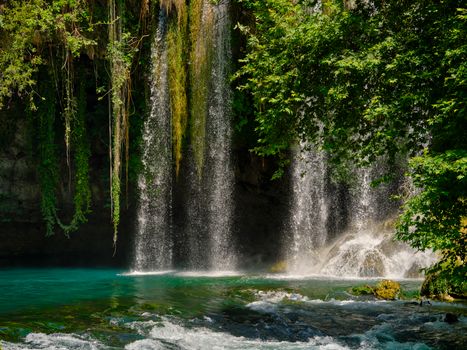 Tranquil waterfall cascading into a clear river, surrounded by lush greenery.