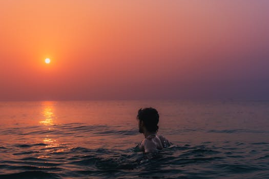 A peaceful moment during sunrise, captured over the ocean in Visakhapatnam, India with a silhouette of a man swimming.