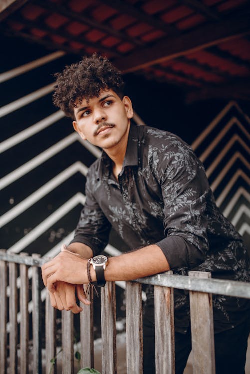 Man with Curly Hair and Mustache Leaning on a Railing