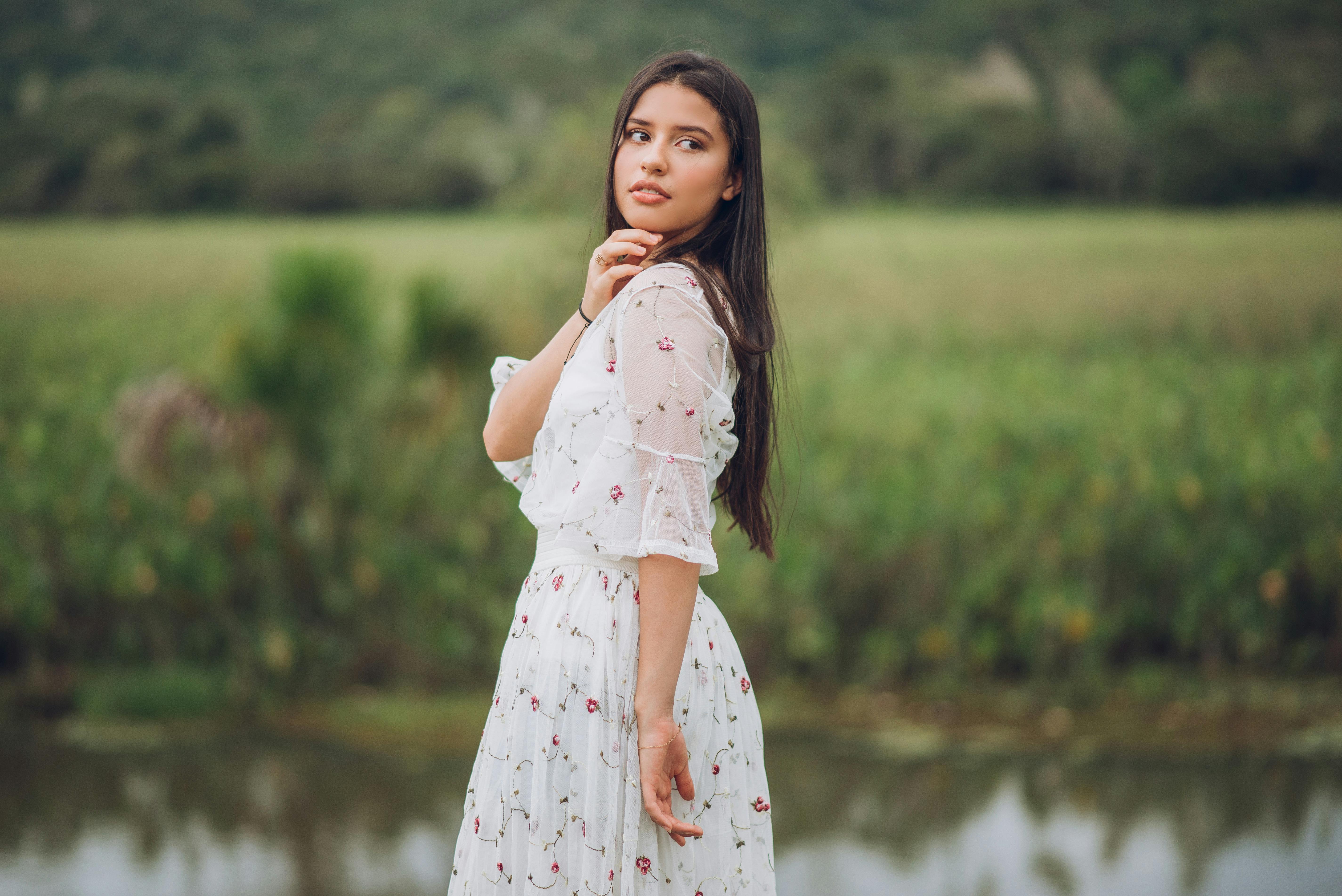 woman in a dress standing next to a lake looking over her shoulder