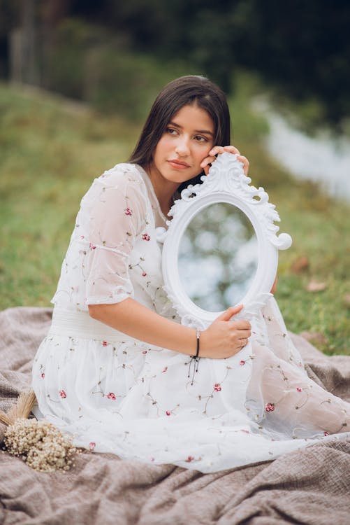 Woman in a Long Dress Sitting on a Blanket Holding a Mirror