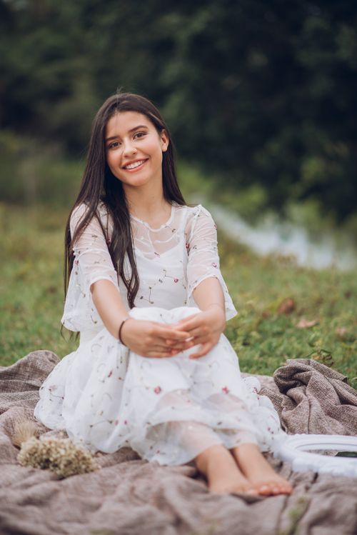 Free Young woman in a dress smiling while sitting on a blanket outdoors in a meadow. Stock Photo