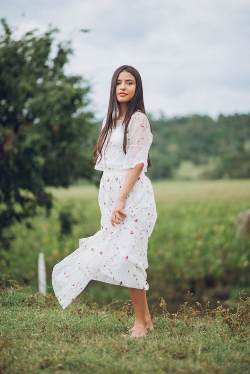 Brunette Woman in a White Dress Barefoot on a Field 
