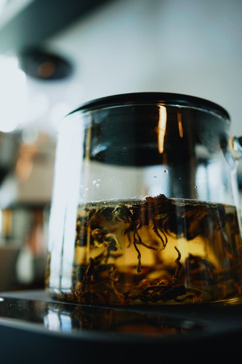 Free Close-up of a glass teapot with green tea leaves steeping, capturing warm tones and reflections. Stock Photo