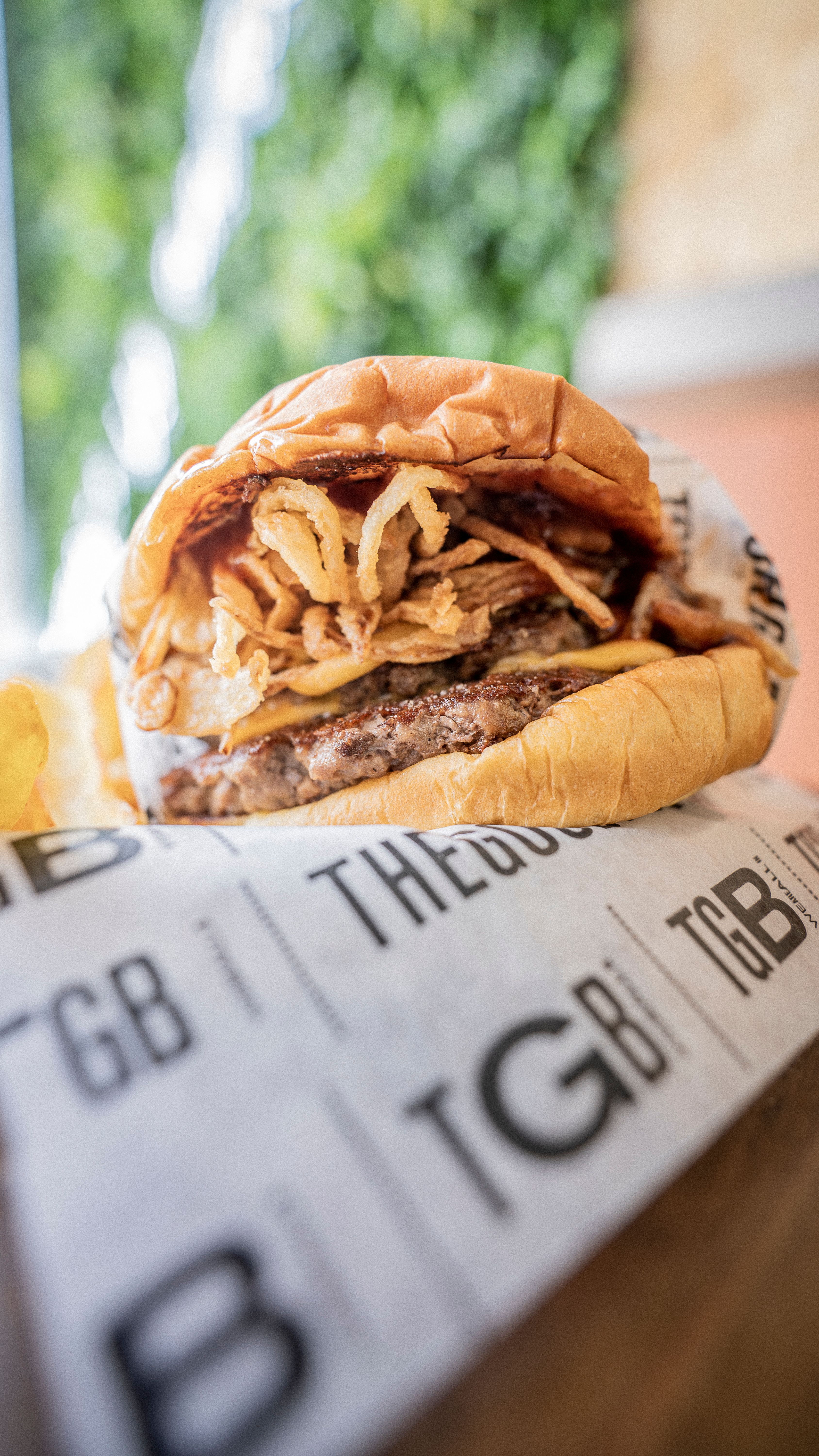 Close-up of a delicious gourmet burger topped with crispy onion rings on branded paper.