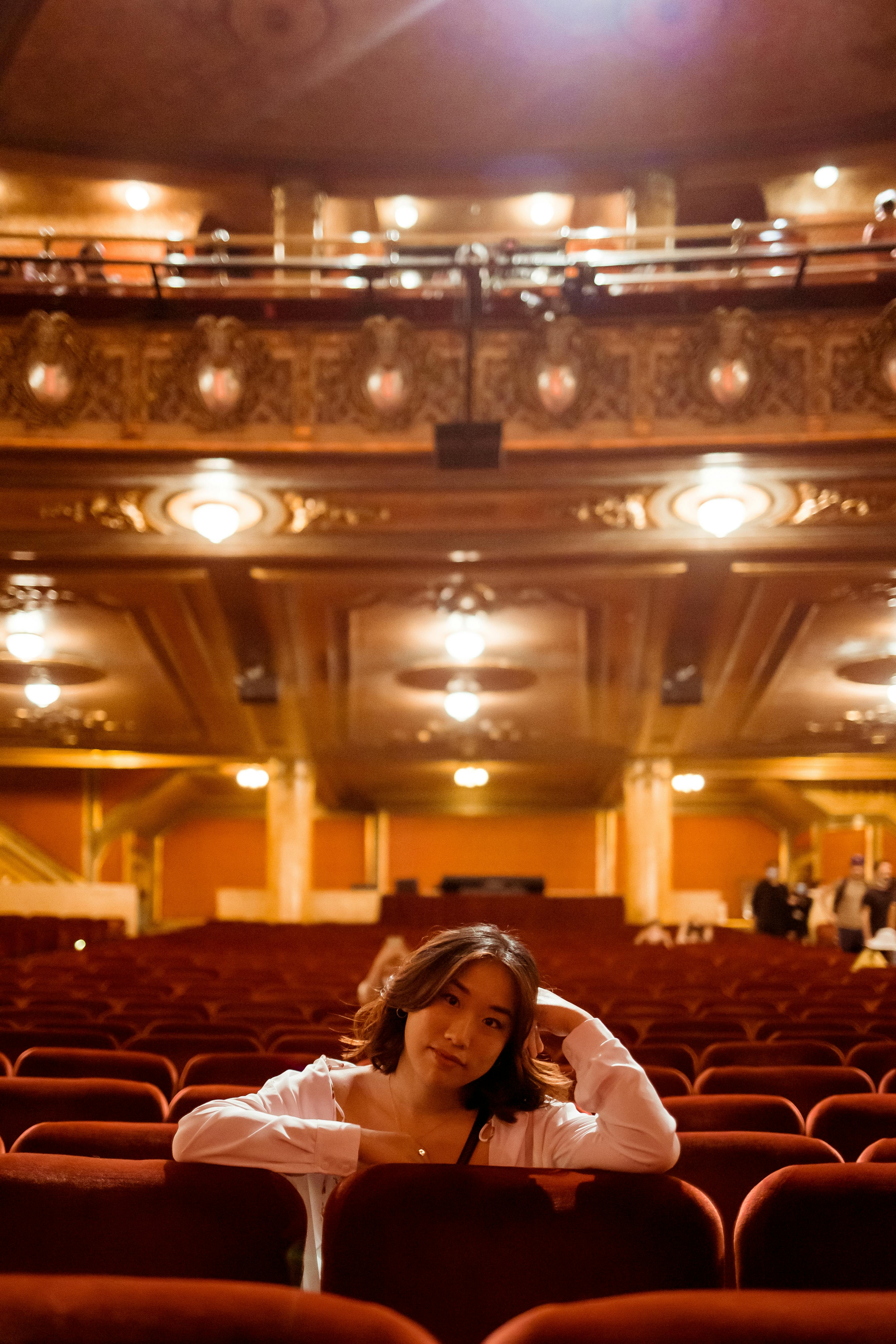 Free A woman sits in an empty theatre with warm lights casting a cozy glow. Stock Photo