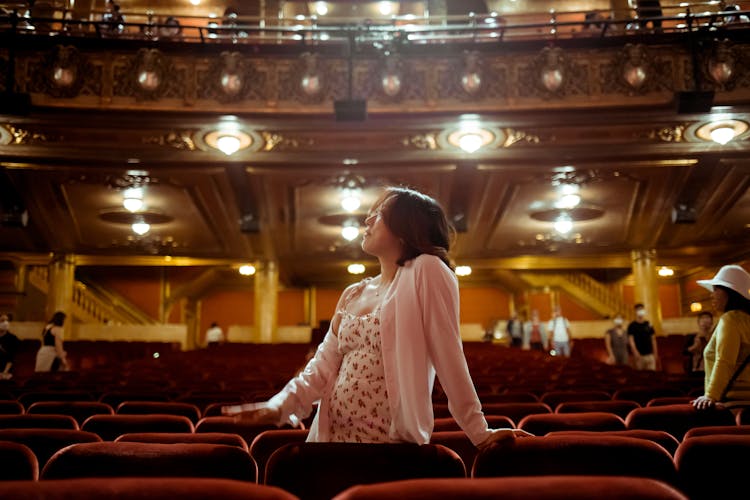 Woman In Dress Posing In Theatre Near Chairs