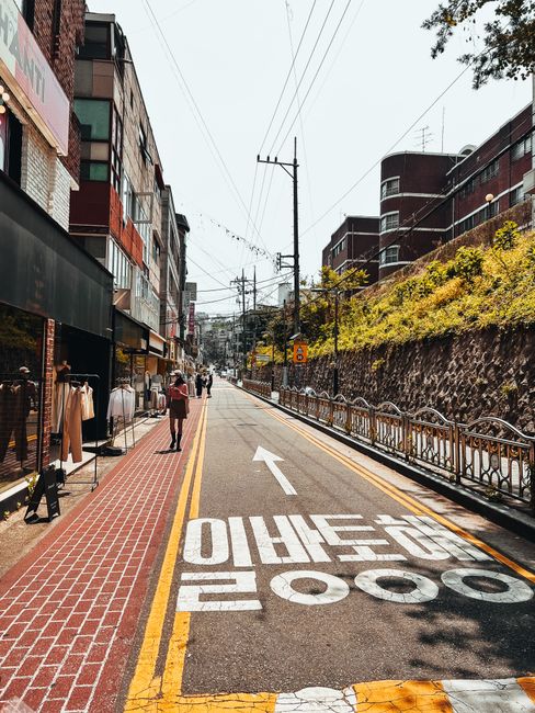 A picturesque urban street featuring shops, buildings, and an empty road under a clear sky.