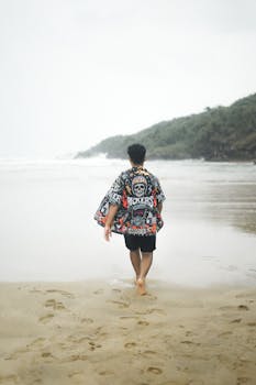 A man in casual attire walks along a tranquil beach on a summer day.