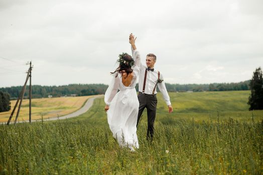Newlywed couple dancing in a picturesque meadow under an overcast sky.