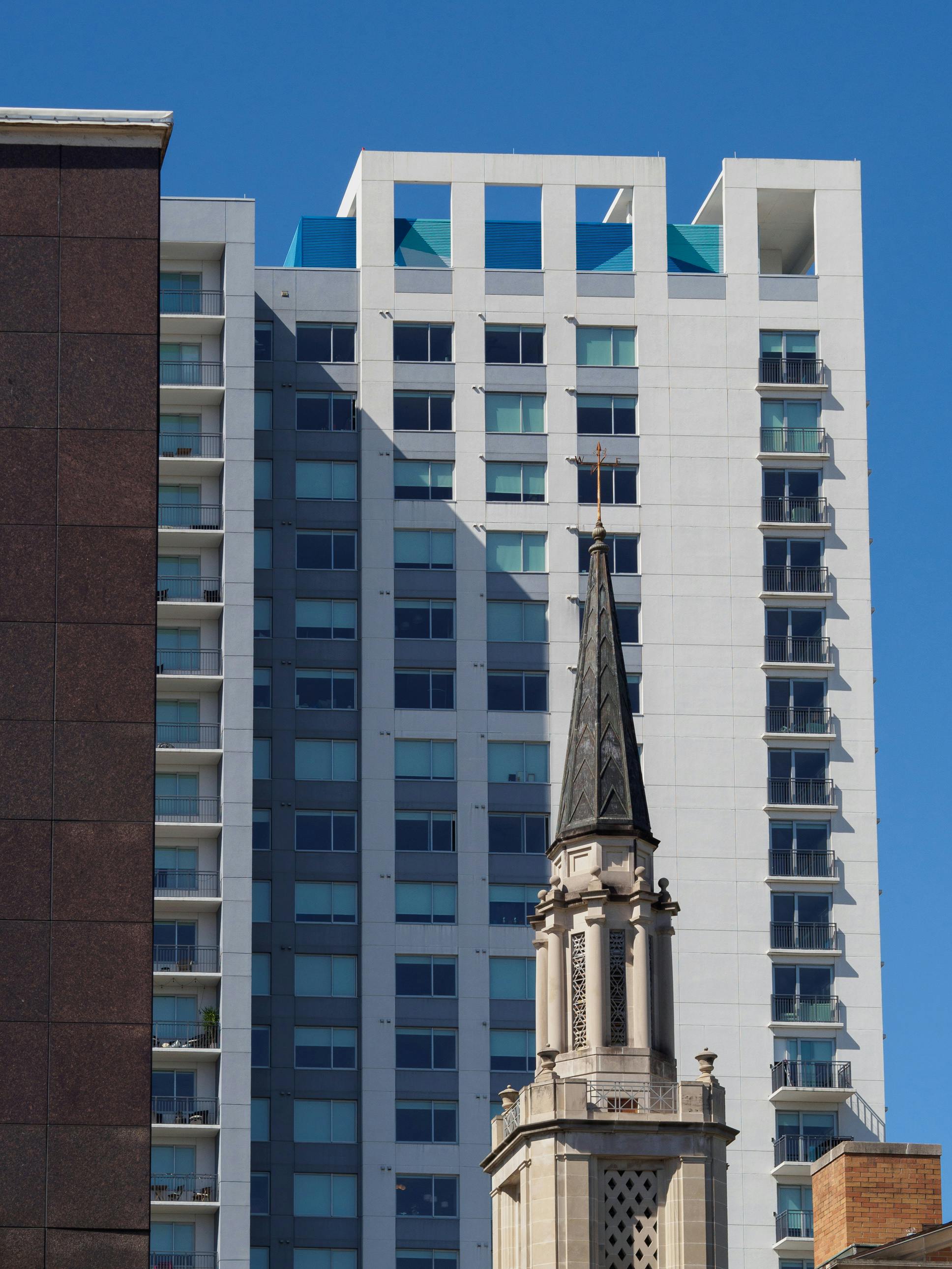 A striking juxtaposition of a church tower against a modern skyscraper under a clear blue sky.