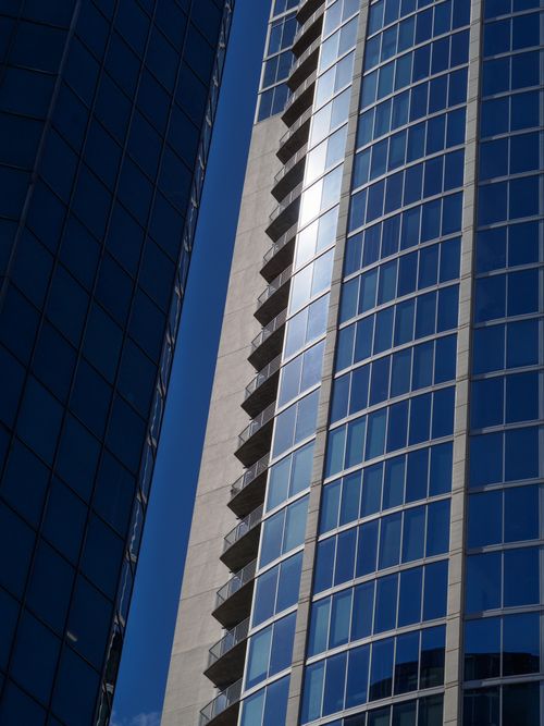 Free Low angle view of a modern skyscraper with reflective glass facade and balconies against a clear blue sky. Stock Photo