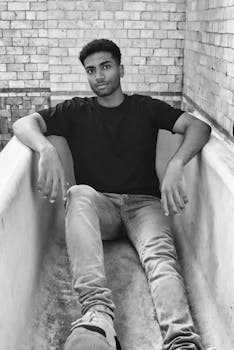 A young man in a black shirt lounging in a vintage bathtub against a brick wall.