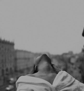 Artistic black and white portrait of a person leaning back, with cityscape background.