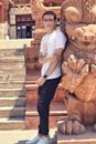 Man in White T-shirt and Black Pants Standing Beside Brown Concrete Statue