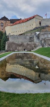 Beautiful reflection of Bečov Castle in a serene pool surrounded by lush greenery.