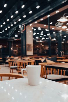 White ceramic mug on a marble table in a warmly lit café with bokeh lights.