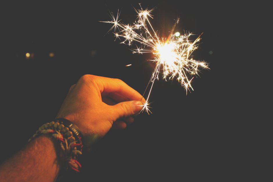 A hand holding a sparkling sparkler in the dark, perfect for festive celebrations.