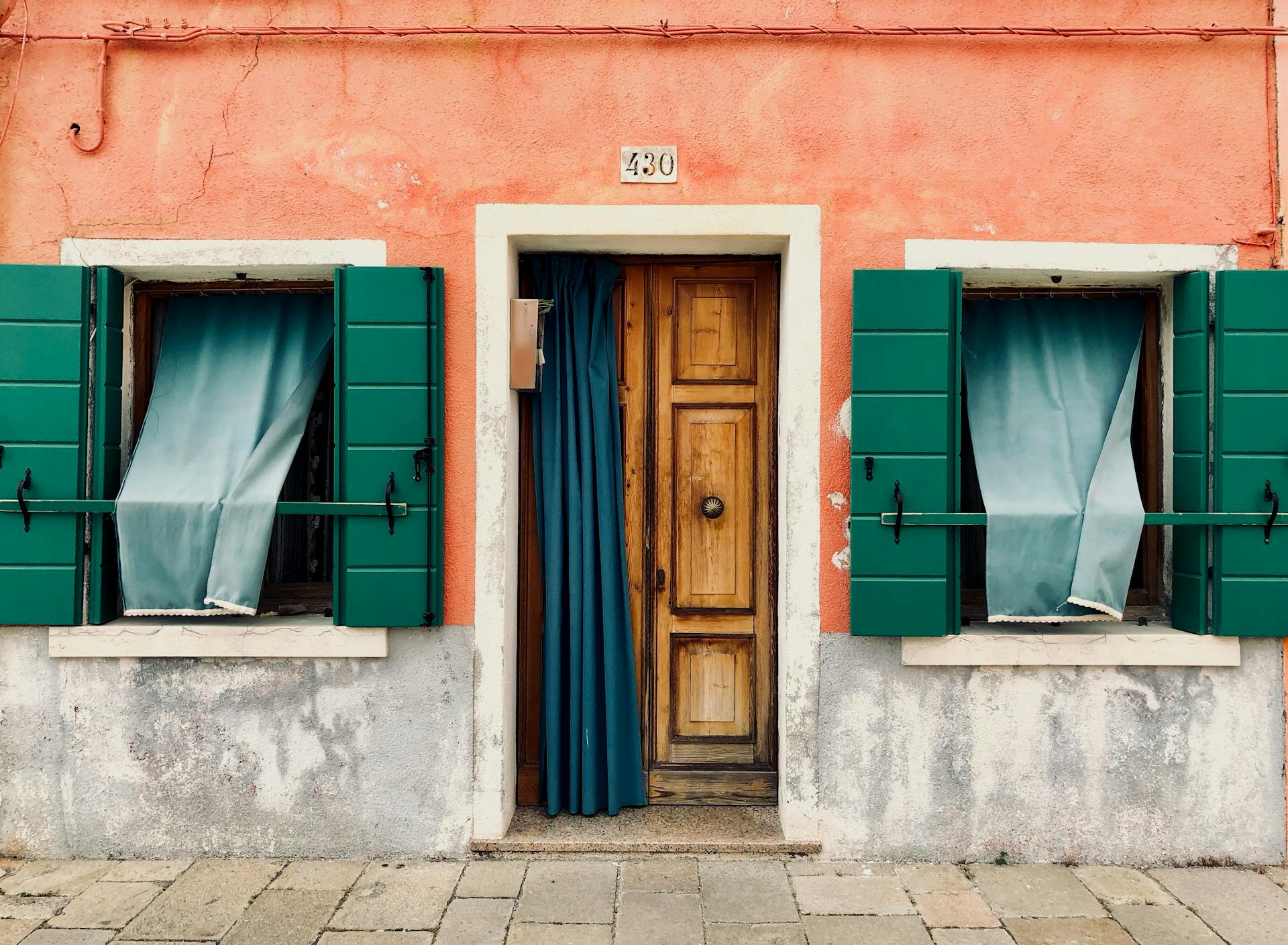 Exterior of a colorful Venetian house with green shutters and a wooden door.
