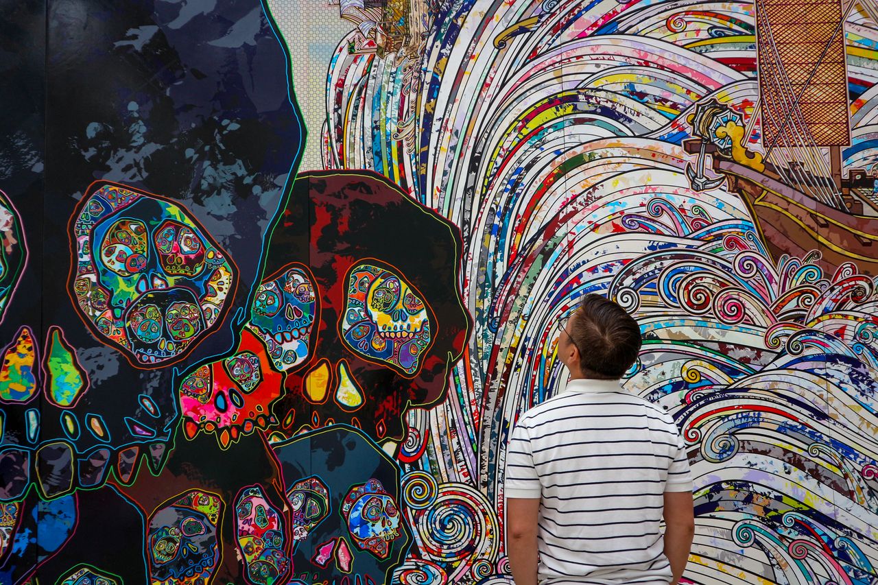 a man in a striped shirt views a colorful mural with intricate skull d