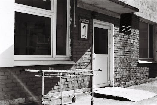 Photo by Oleg PavLove Monochrome image of a hospital entrance featuring a gurney and a brick building.