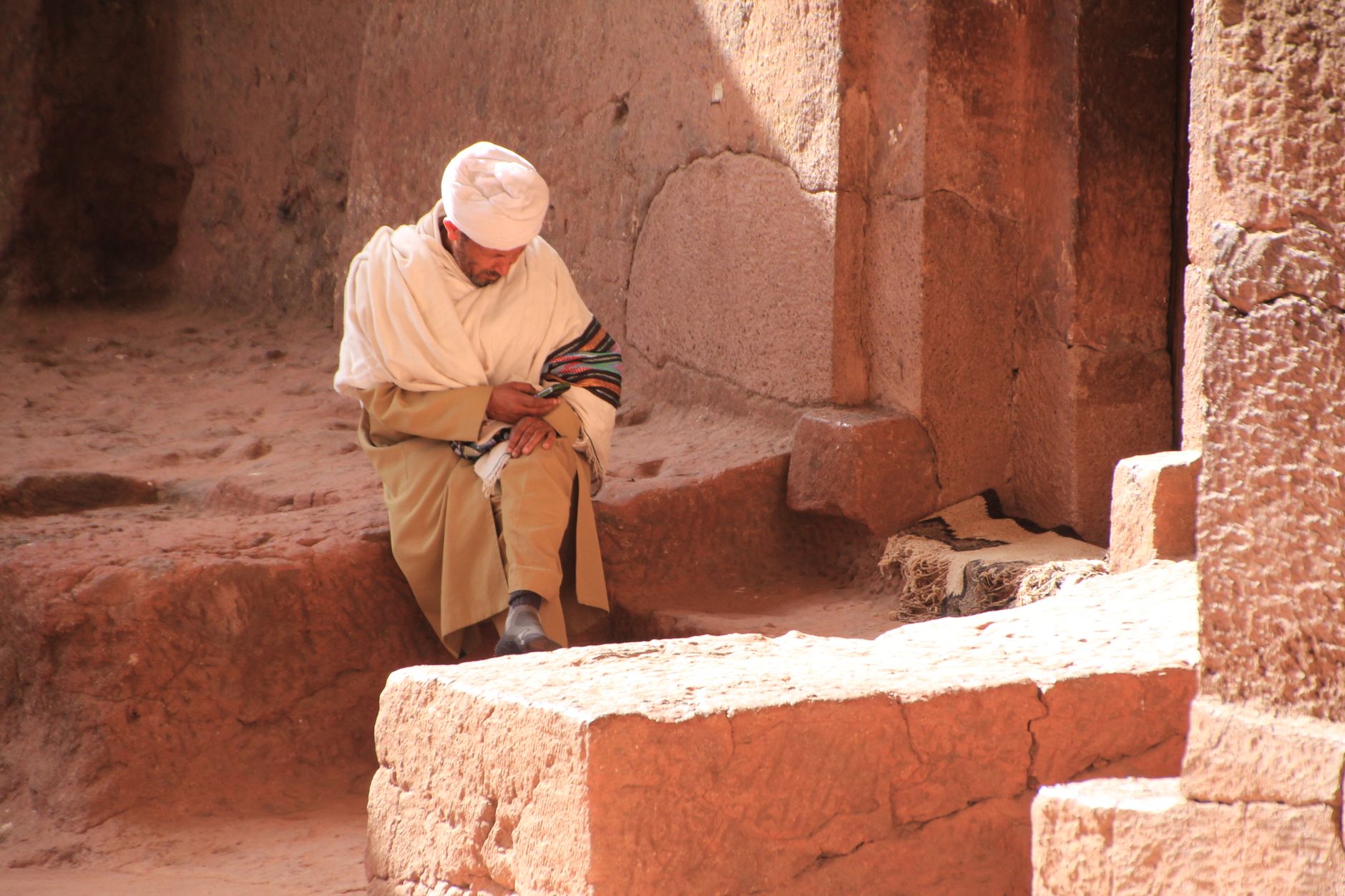 A man in traditional attire sitting within the ancient rock-hewn churches of Lalibela, Ethiopia.