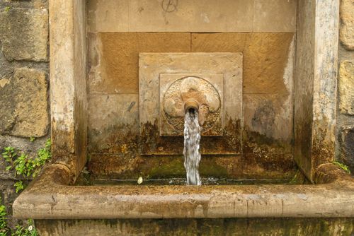 Free Rustic stone fountain pouring water, creating a vintage outdoor ambiance. Stock Photo