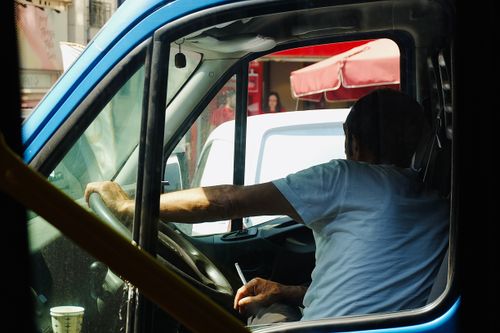 Free Side view of a man sitting in a parked vehicle, smoking, under sunlight streaming through the window. Stock Photo