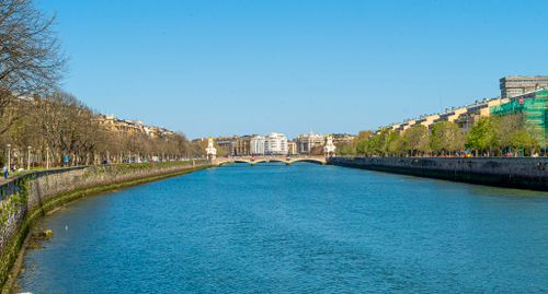 Free A peaceful view of a river flowing through a city with a picturesque bridge and vibrant greenery. Stock Photo