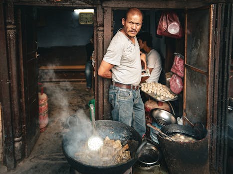 A man cooking street food in a bustling outdoor setting, showcasing traditional culinary methods.
