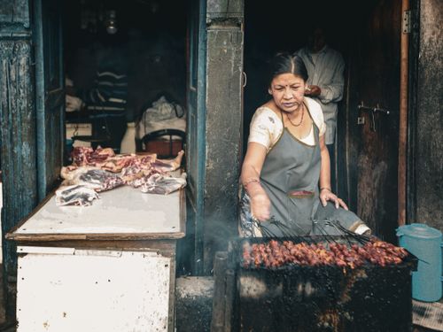 Free Woman grilling meat skewers at a bustling outdoor street market. Stock Photo
