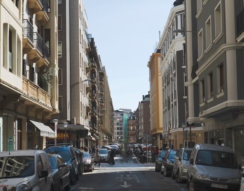 Free A bustling city street lined with parked cars and buildings under a clear sky. Stock Photo