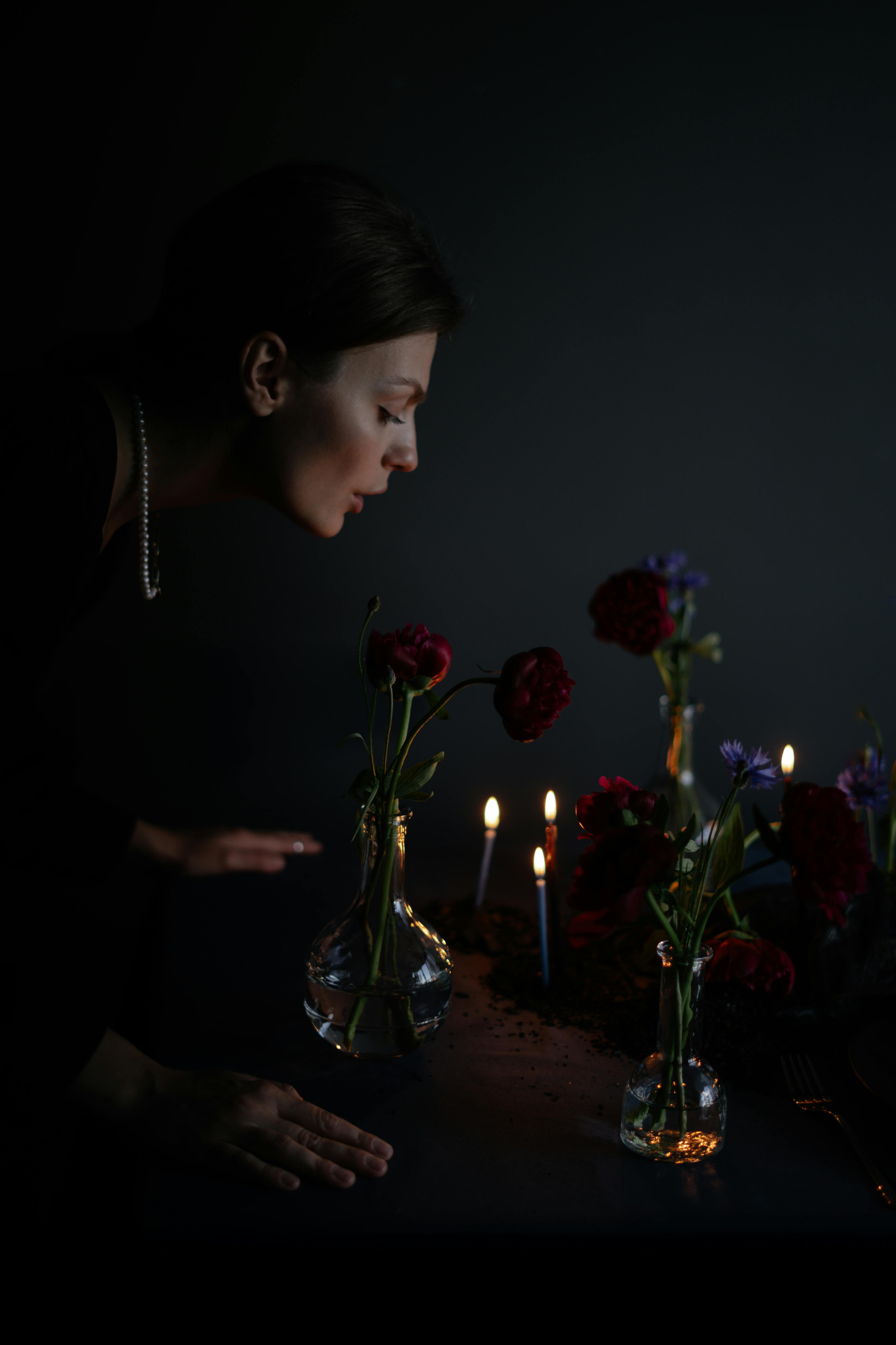 A woman admiring flowers in a dark, candlelit setting, creating a moody and elegant atmosphere.