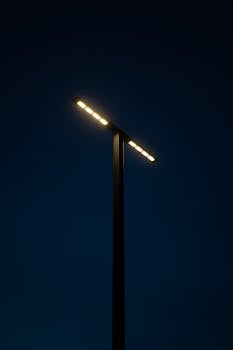 A modern street lamp illuminates the dark night sky with a minimalist design.