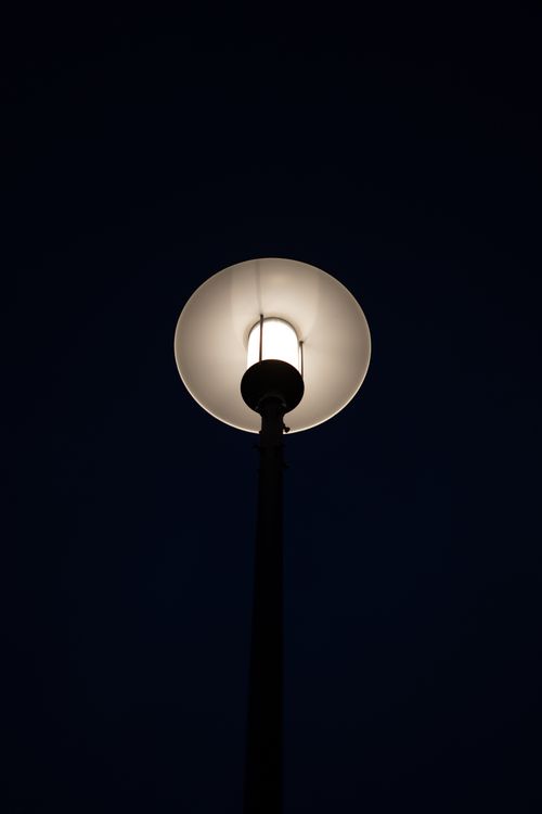 Free A glowing street lamp shines against a dark, expansive night sky, creating a serene and moody atmosphere. Stock Photo