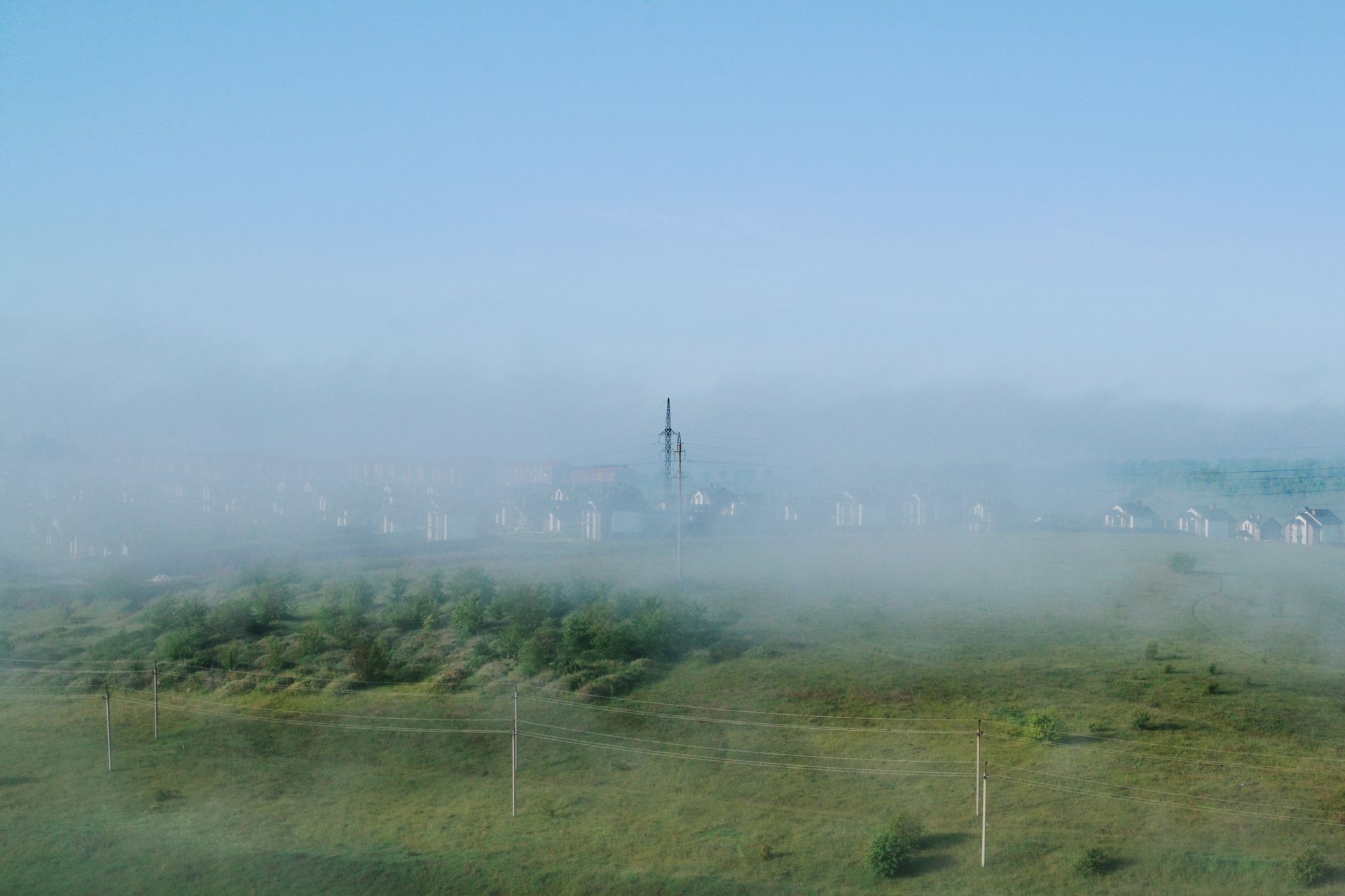 A tranquil rural scene with mist over fields and distant houses under a clear sky.