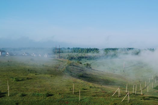 A serene aerial view of a misty countryside landscape with grasslands and distant houses.