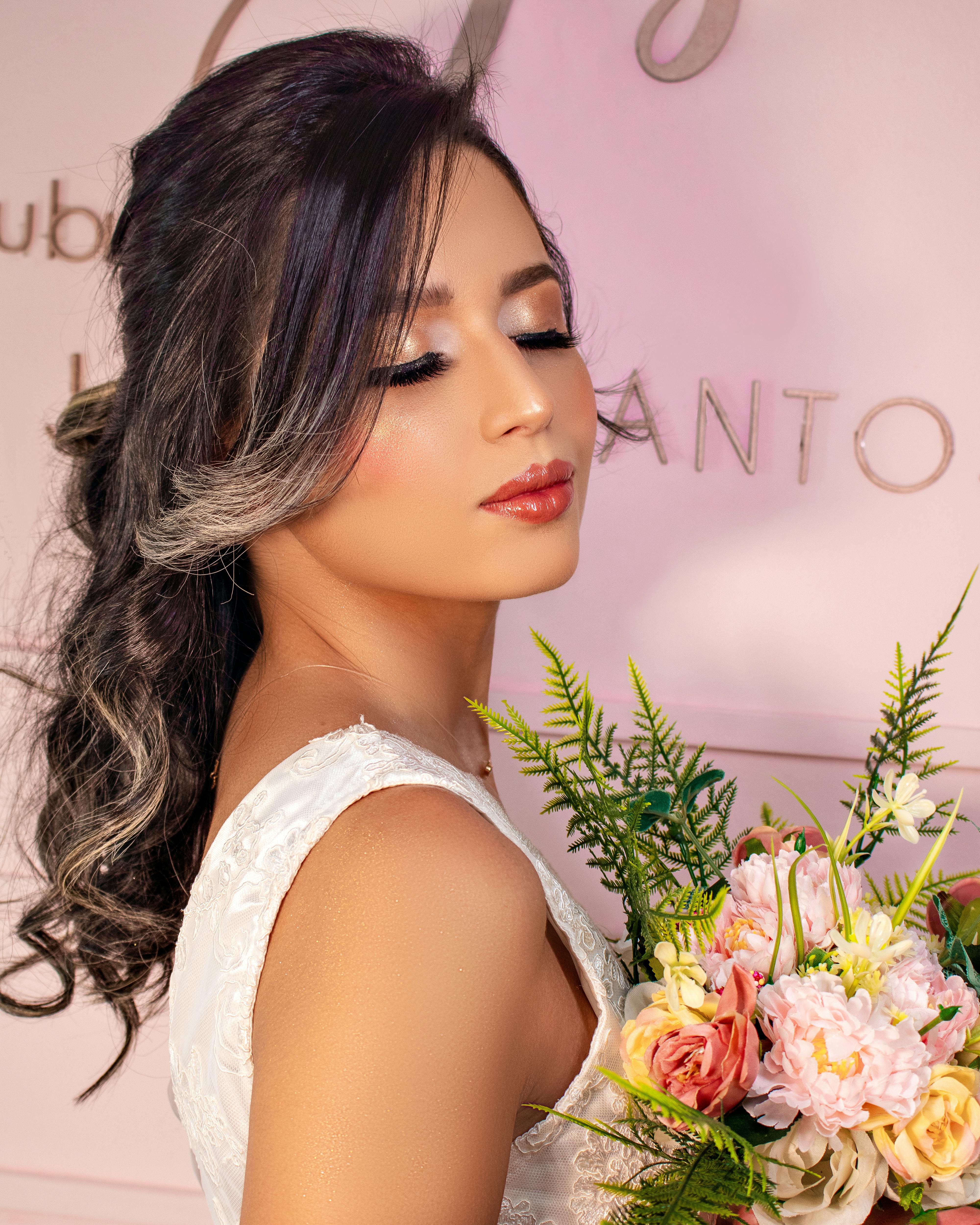 Beautiful brunette woman in a white dress holding a floral bouquet, exuding elegance and glamour.