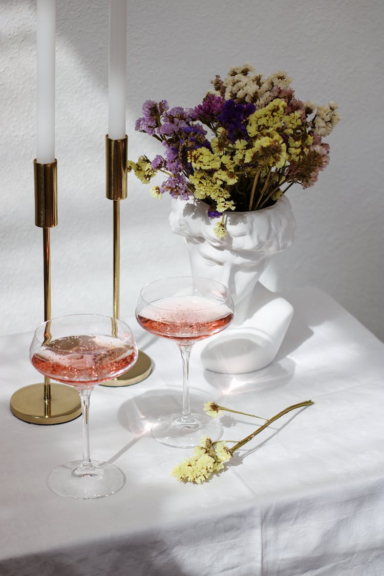 Sculpture Pot With Flowers, Glasses With Drink And Candles On Table