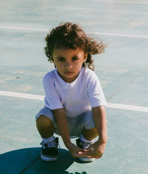 Free A young child crouching on an outdoor sports court, capturing a moment of leisure and playfulness. Stock Photo