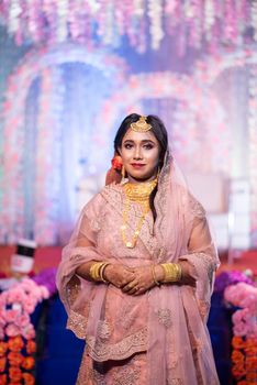 A beautiful Indian bride in traditional attire, richly adorned with jewelry and intricate henna, posing elegantly indoors.