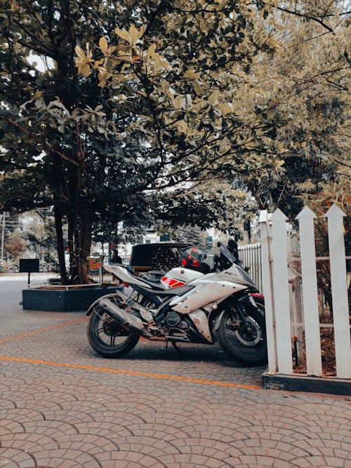 White and Black Motorcycle Parked Beside the White Wooden Fence