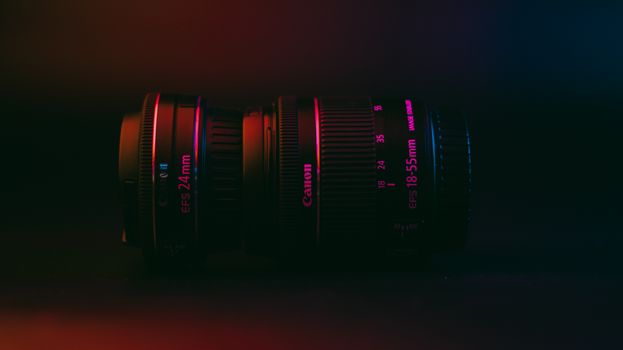 Moody close-up of Canon 24mm and 18-55mm lenses under vibrant lighting.