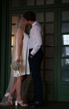 Intimate portrait of a newlywed couple kissing, with the bride holding a bouquet and wearing a veil.