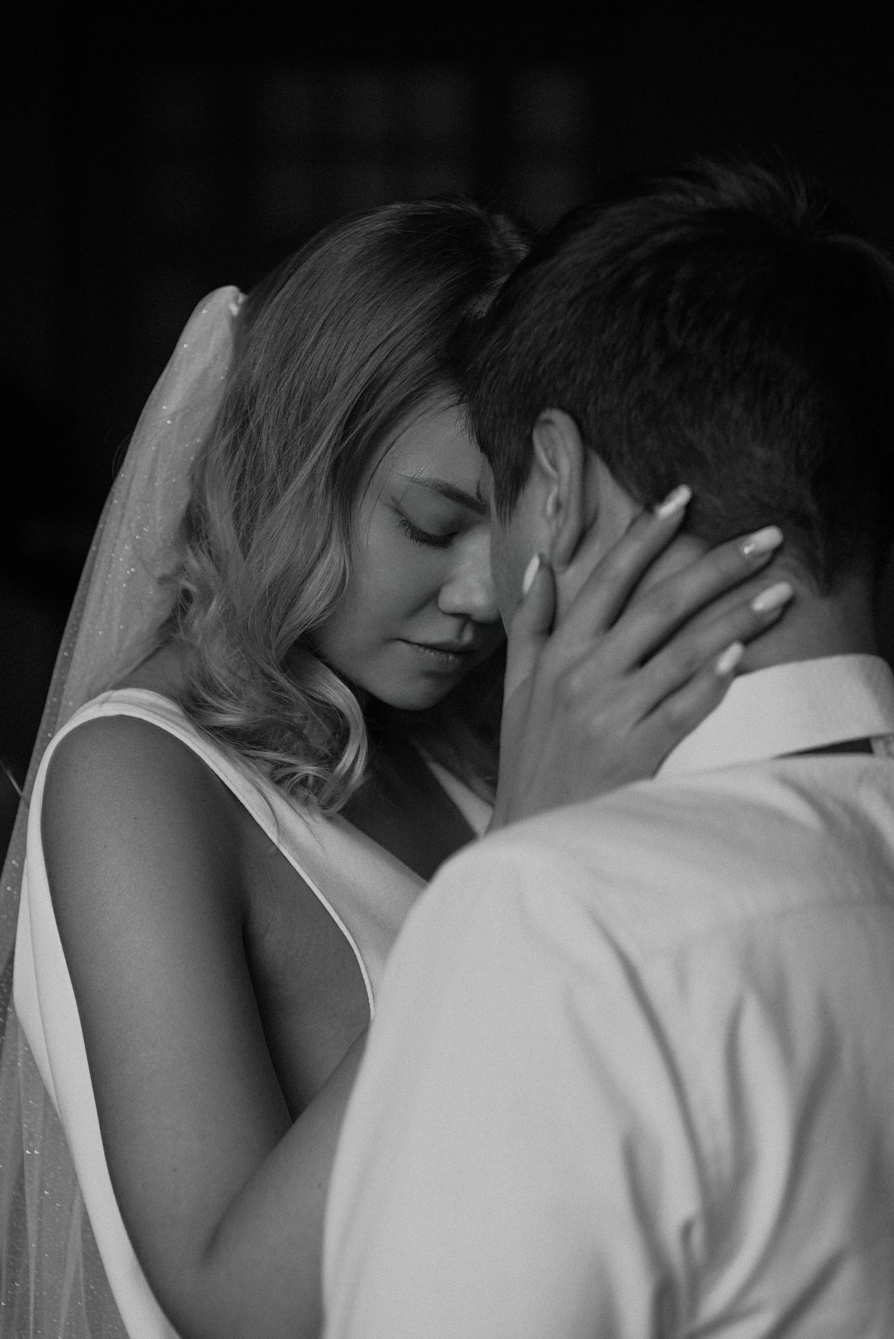 Intimate black and white portrait of a bride and groom sharing a tender moment.