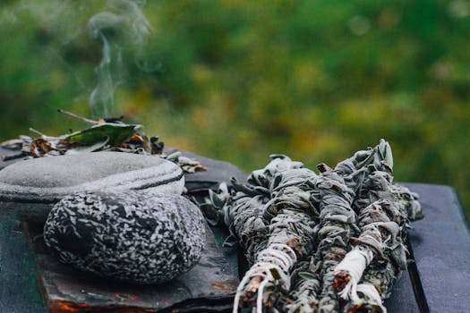 Herbal sage smudge and steaming hot stones on a wooden table in a natural outdoor setting.