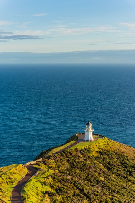 Scenic view of Cape Reinga Lighthouse at sunset in Northland, New Zealand, surrounded by ocean.