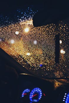 View through a rainy car windshield at night, highlighting raindrops and blurred city lights.