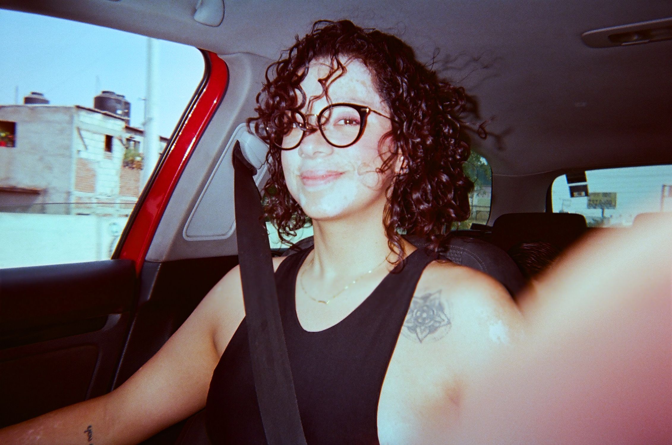 Woman with eyeglasses driving in Cuernavaca, Mexico, wearing a black tank top and smiling.