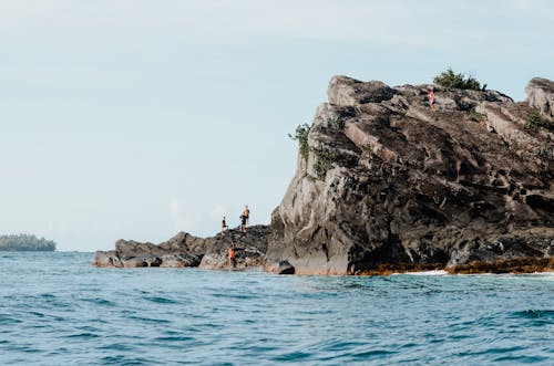 People Swimming on Sea Near Rocky Mountain